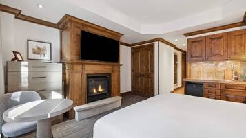 A hotel room with a fireplace, a television, a dining area, and a kitchen.