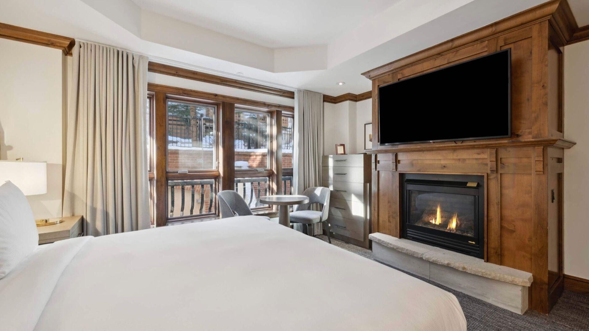 A hotel room with a large bed, a fireplace, a television, and a balcony with a view of the outside.