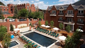 A hotel with a swimming pool, lounge chairs, and a red brick building in the background.