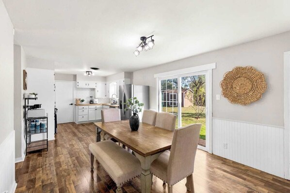 Une cuisine moderne avec des meubles blancs, un réfrigérateur en acier inoxydable et un coin repas comprenant une table et des chaises en bois.