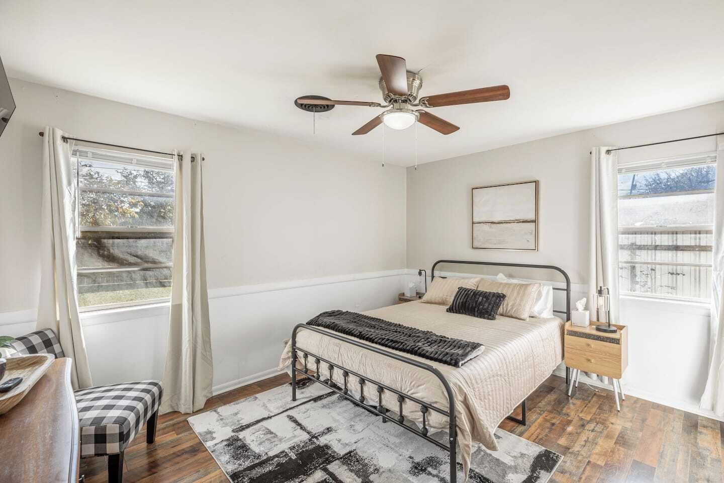 Un dormitorio con cama, ventilador de techo, mesita de noche, silla y ventana.