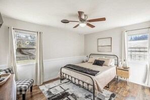 Une chambre à coucher avec un lit, un ventilateur de plafond, une table de chevet, une chaise et une fenêtre.