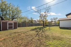 A backyard with a shed, a fenced area, and a tree. - 3 Queen Beds • Full Kitchen • Ideal for Long Stays (Abilene)
