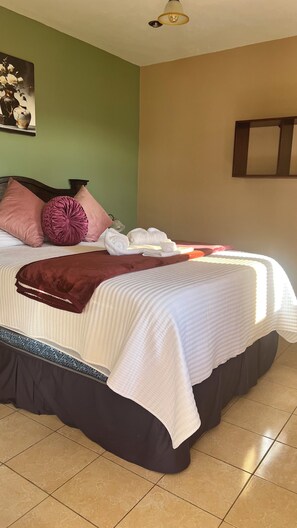A neatly made bed with a white comforter, a dark skirt, and pink pillows. - Hotel El Tambor OASIS Antigua Guatemala (Antigua Guatemala)
