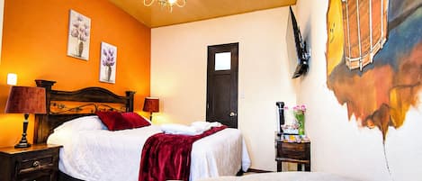 Una habitación de hotel con una cama, mesitas de noche, una lámpara, un cuadro en la pared y una puerta.