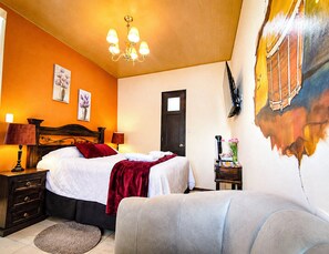 A hotel room with a bed, bedside tables, a lamp, a painting on the wall, and a door. - Hotel El Tambor OASIS Antigua Guatemala (Antigua Guatemala)