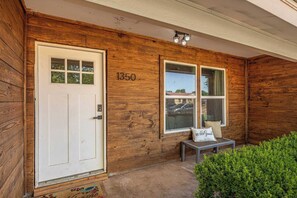 A wooden exterior with a white door, two windows, and a bench with a cushion. - Spacious 4BR with Long Kitchen and Relaxing Patio (Abilene)