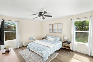 Ein Schlafzimmer mit einem Bett, Nachttischen, einem Deckenventilator und einem Fenster mit Vorhängen.