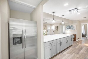 A modern kitchen with a stainless steel refrigerator, white cabinetry, and a large island. - Spacious 4BR with Long Kitchen and Relaxing Patio (Abilene)