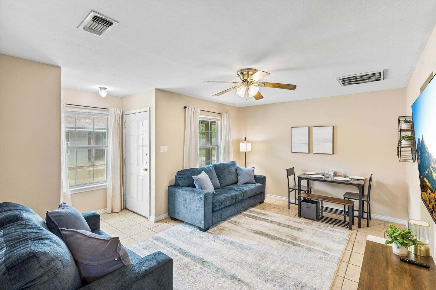Ein Wohnzimmer mit einer Couch, einem Esstisch mit Stühlen, einem Deckenventilator und einem Bild an der Wand.