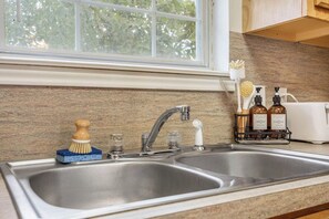 A kitchen with a double stainless steel sink, a window above it, and a countertop with a dish soap dispenser and a hand soap dispenser.