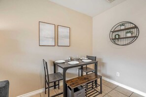 Un coin repas avec une table dressée pour deux personnes, deux tableaux encadrés au mur et une étagère circulaire ornée de plantes.