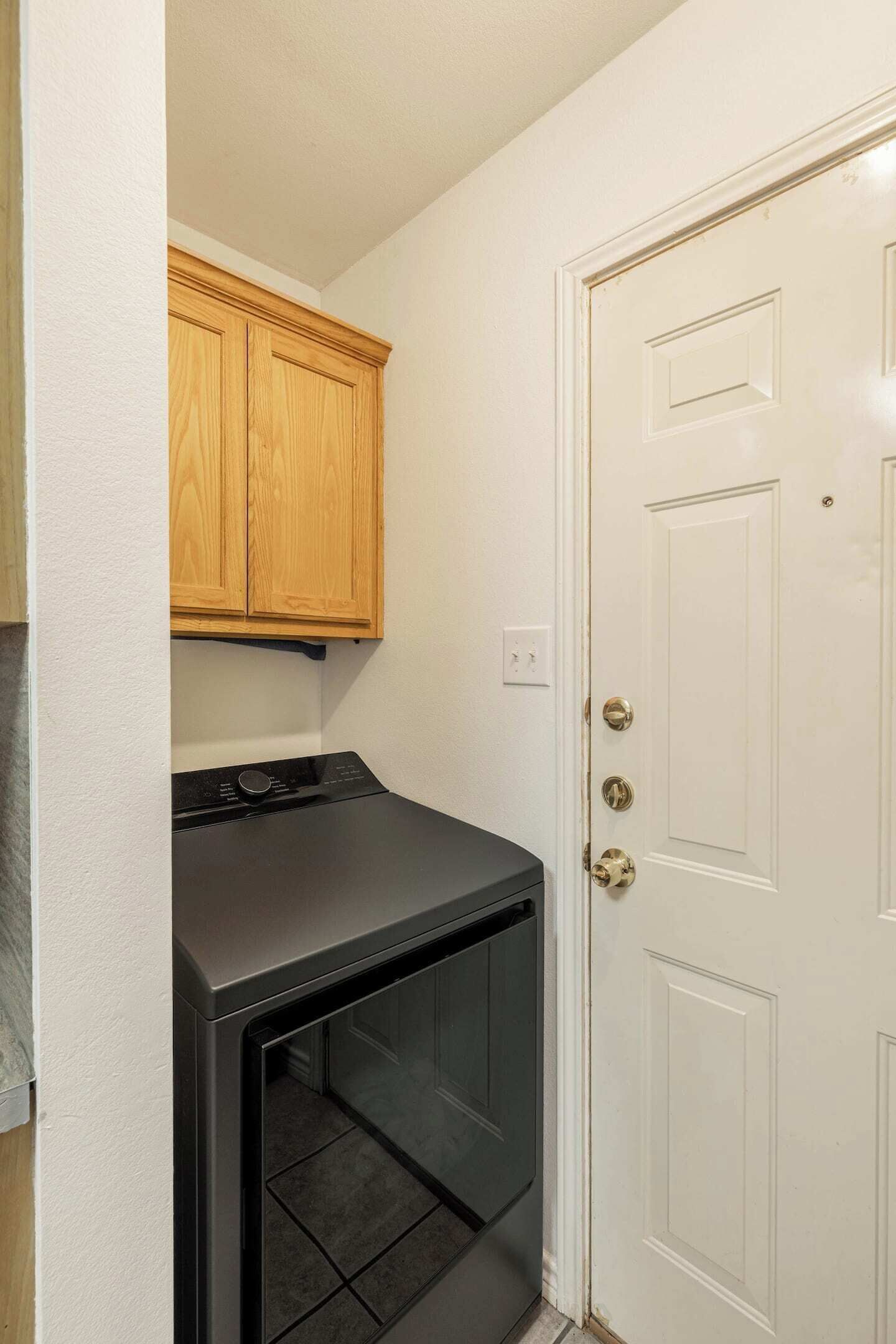 A laundry room with a black washer and dryer, wooden cabinets, and a white door.
