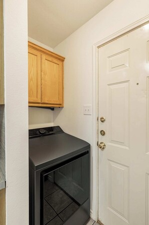 A laundry room with a black washer and dryer, wooden cabinets, and a white door.