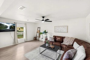 Ein modernes Wohnzimmer mit einem braunen Ledersofa, einem Glastisch und einem Deckenventilator.