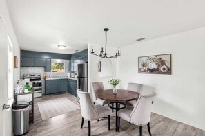 Une cuisine moderne avec des meubles de couleur sombre, un réfrigérateur en acier inoxydable et un coin repas comprenant une table ronde et quatre chaises.