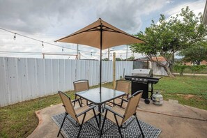 Une terrasse extérieure avec une table et des chaises, un barbecue et une guirlande lumineuse.