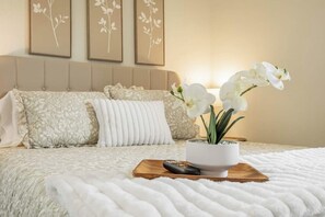 Une chambre à coucher avec un lit, des oreillers, une télécommande et une orchidée en pot.
