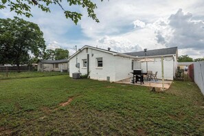 Ein weißes eingeschossiges Haus mit überdachter Terrasse, Grill und umzäunter Garten.