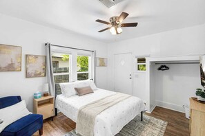 Une chambre à coucher comprenant un lit, un bureau, une chaise, un ventilateur de plafond et une fenêtre avec des rideaux.
