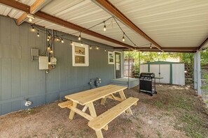 Une terrasse extérieure avec une table et des bancs en bois, un barbecue et des guirlandes lumineuses.