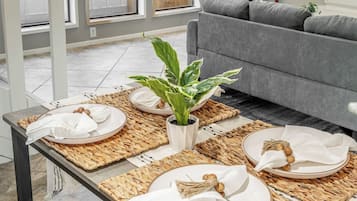 A dining area with a table set for four, a grey sofa, and a large window with blinds.