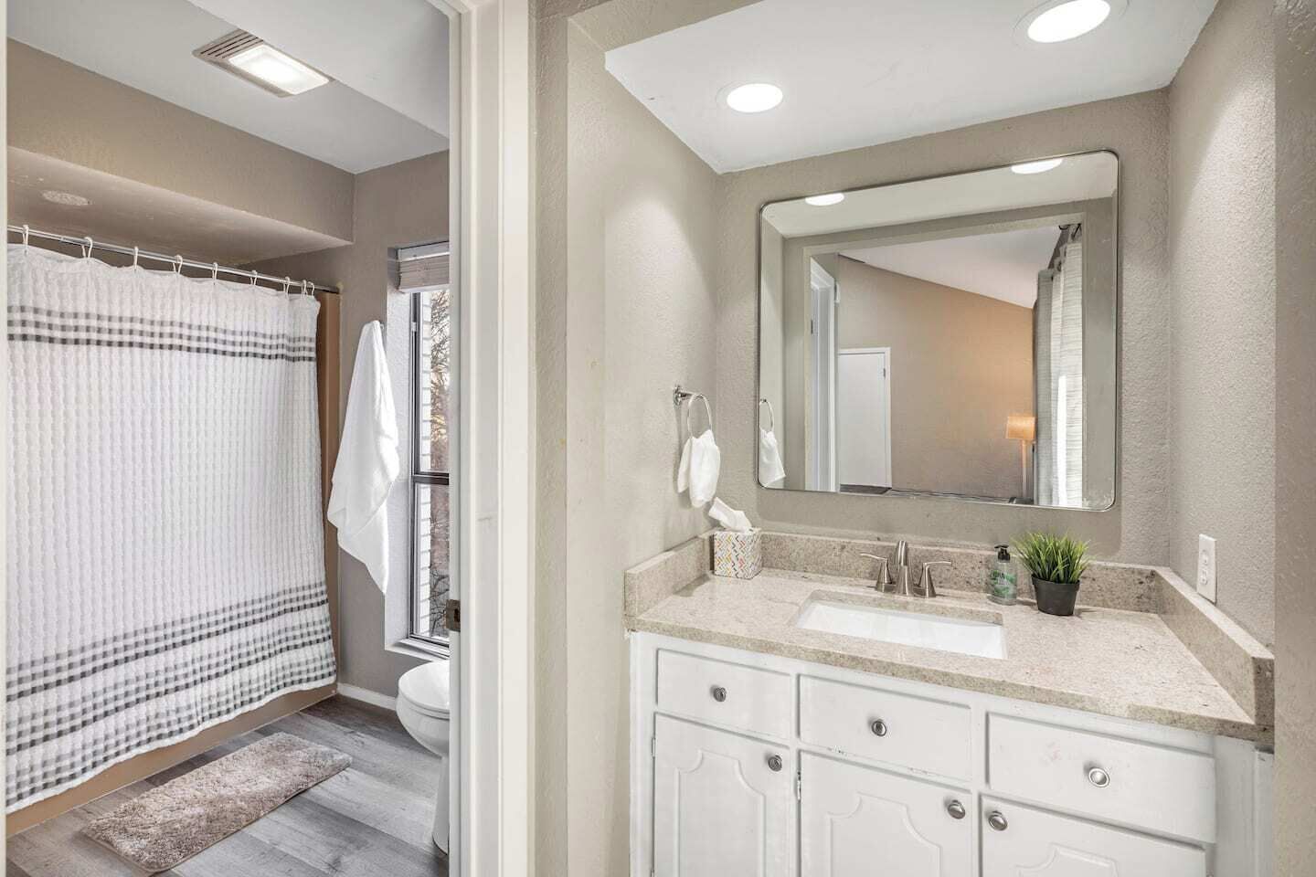 A bathroom with a shower, toilet, sink, and mirror.