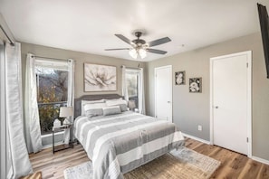 Une chambre à coucher avec un lit, un ventilateur de plafond, une fenêtre avec des rideaux et une porte.