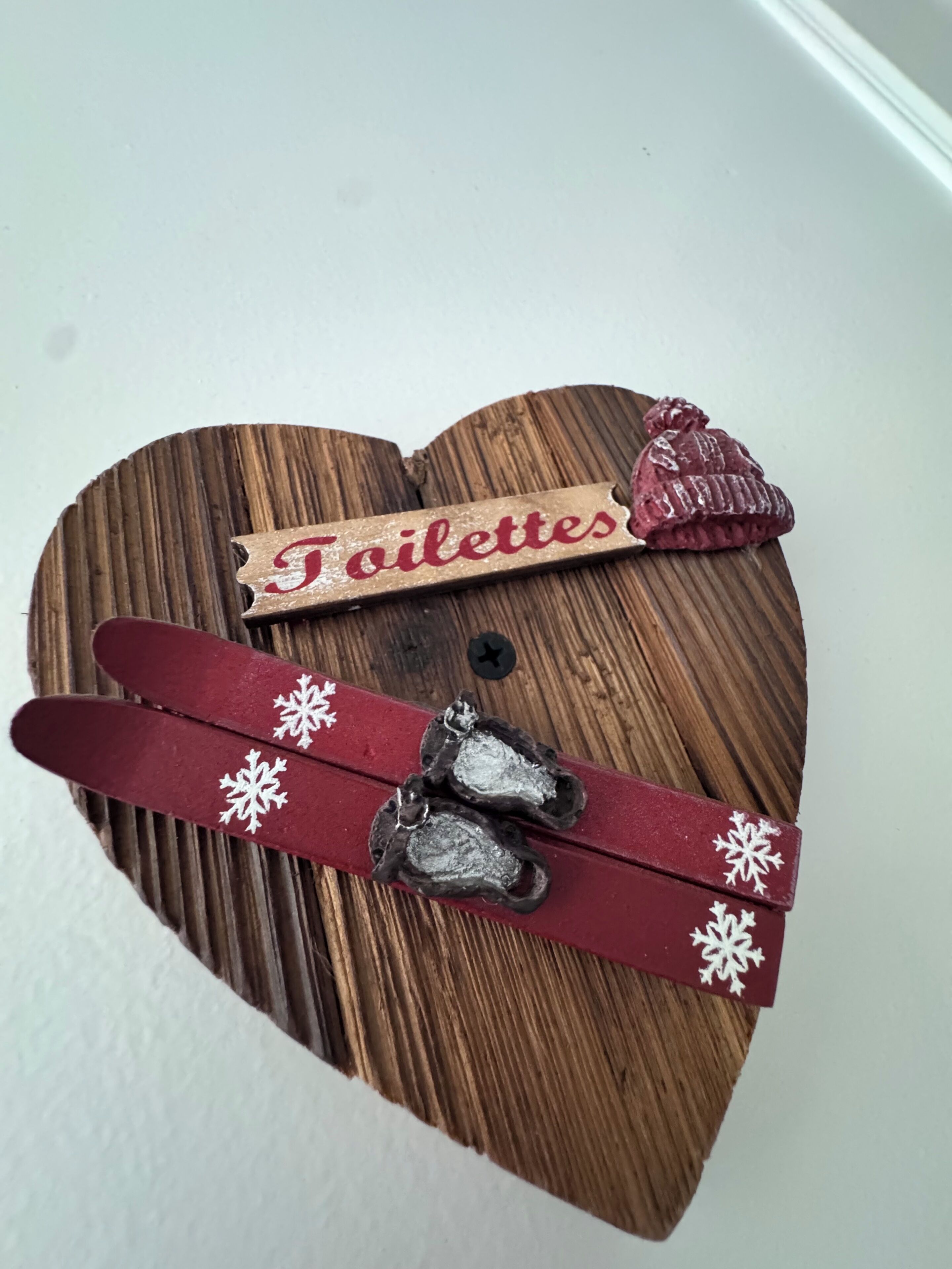 Un letrero de madera con forma de corazón que dice 'Toilettes' e incluye un icono de esquí.
