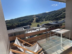 Un balcon avec un hamac, une table en verre et une vue sur un paysage vallonné parsemé de bâtiments.