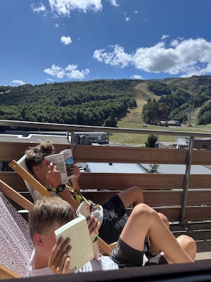 Zwei Personen sitzen auf einer Holzdielen-Terrasse mit Blick auf eine hügelige Landschaft.