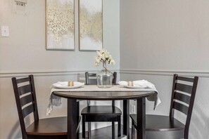 A dining area with a round table, four chairs, a vase with flowers, and two framed artworks on the wall. - Relaxing 2BR House w/ Indoor Spa & Game Room (Abilene)