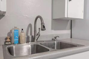 Eine Spüle aus Edelstahl mit modernem Wasserhahn, einem Seifenspender und einer Flasche Flüssigseife.