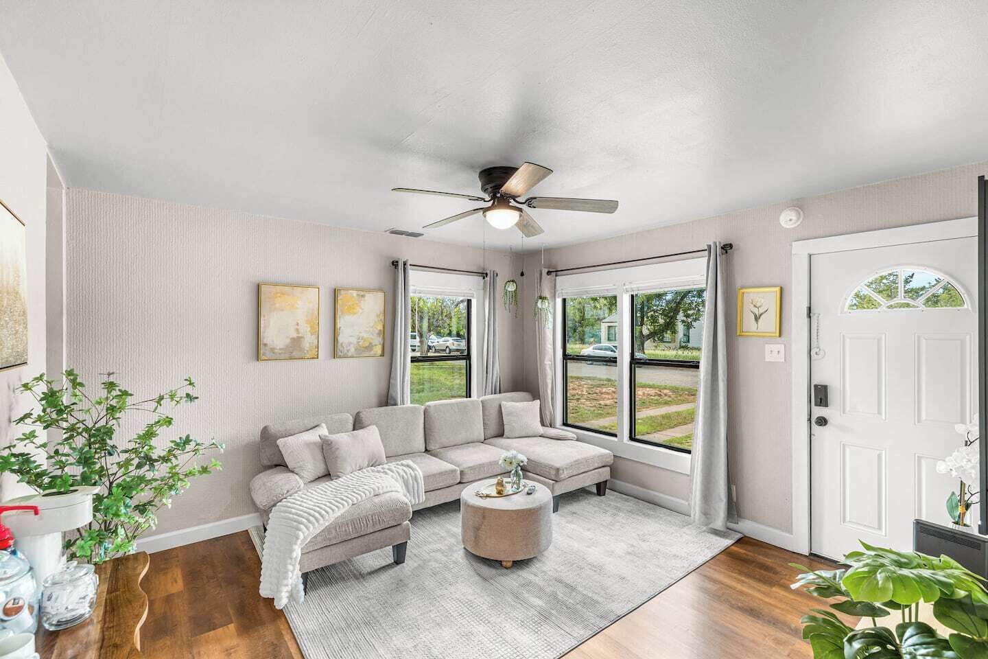 A living room with a sectional sofa, a ceiling fan, and large windows.