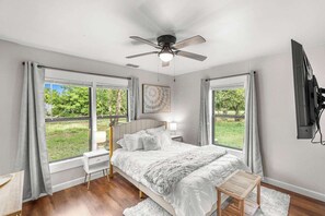 Ein Schlafzimmer mit einem Bett, einem Deckenventilator, einem Fernseher und großen Fenstern.