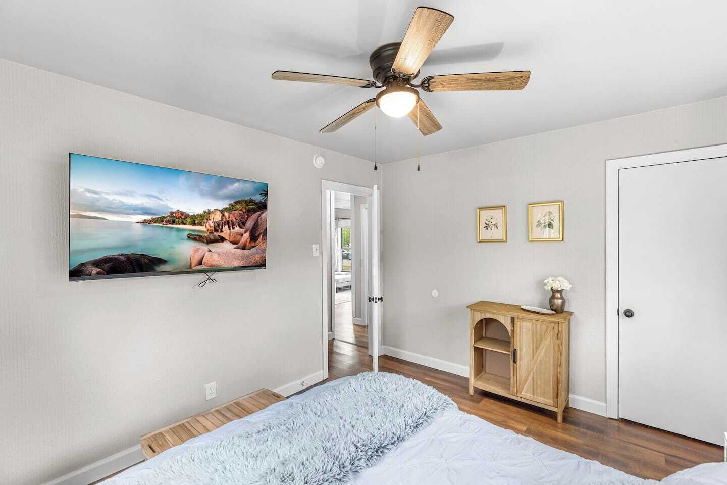 Ein Schlafzimmer mit einem Bett, einem Deckenventilator, einem an der Wand befestigten Fernseher und einem Holzschrank.