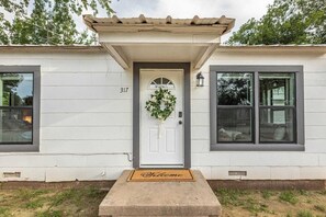 A white building with a number 317, a front door with a wreath, and a welcome mat. - Relaxing 2BR House w/ Indoor Spa & Game Room (Abilene)