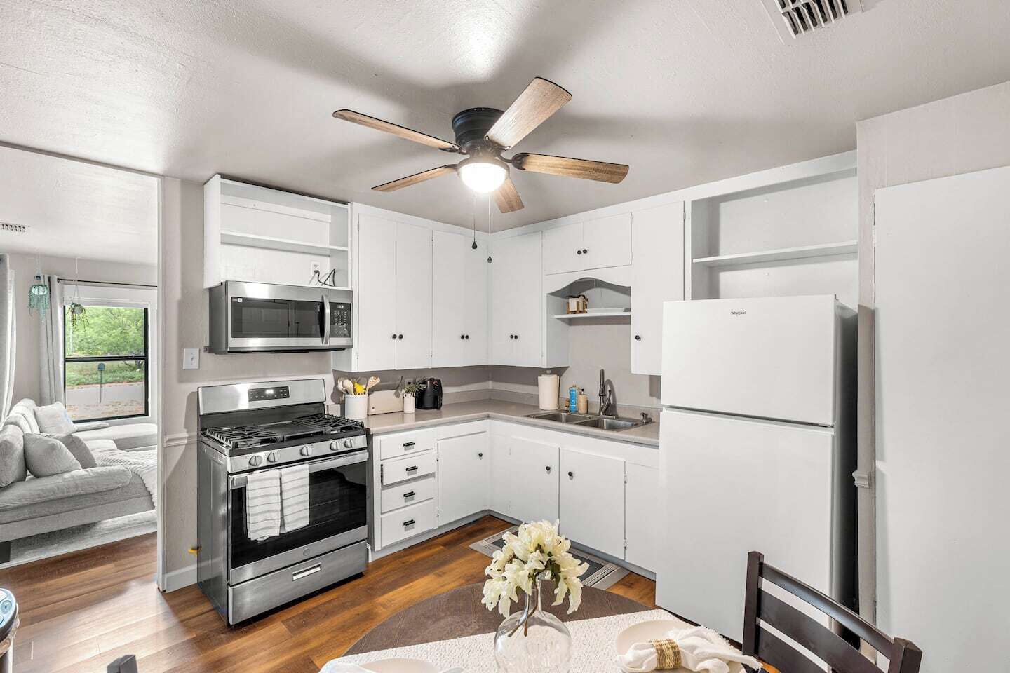Une cuisine moderne avec des meubles blancs, une cuisinière en acier inoxydable, un four à micro-ondes et un ventilateur de plafond.