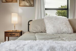 A bed with a fluffy white pillow, a bedside table with a lamp, and artwork on the wall. - Relaxing 2BR House w/ Indoor Spa & Game Room (Abilene)