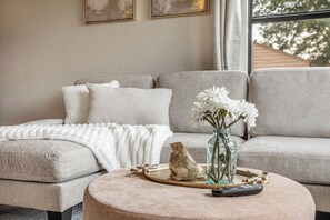 A living room with a sofa, ottoman, and decorative items including a vase with flowers and a bird sculpture. - Relaxing 2BR House w/ Indoor Spa & Game Room (Abilene)