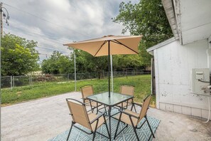 Eine Außenpatio mit einem Glastisch und Stühlen, einem beigen Sonnenschirm und einer Steckdose an der Wand.
