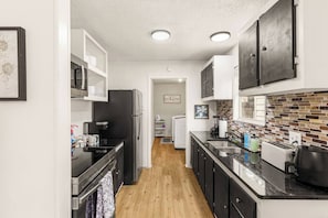A compact kitchen with a refrigerator, stove, and sink, featuring a tiled backsplash and wooden flooring.