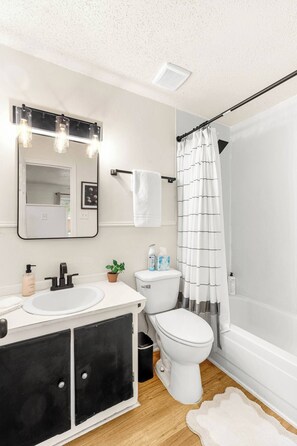 Une salle de bain avec un lavabo blanc, un meuble noir, des toilettes blanches et un rideau de douche.