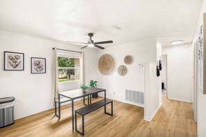 Une chambre moderne avec un ventilateur de plafond, une fenêtre avec des rideaux, une table avec des bancs et des œuvres d’art accrochées au mur.