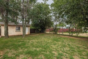 A residential backyard with a house, a fenced area, and a dirt path.