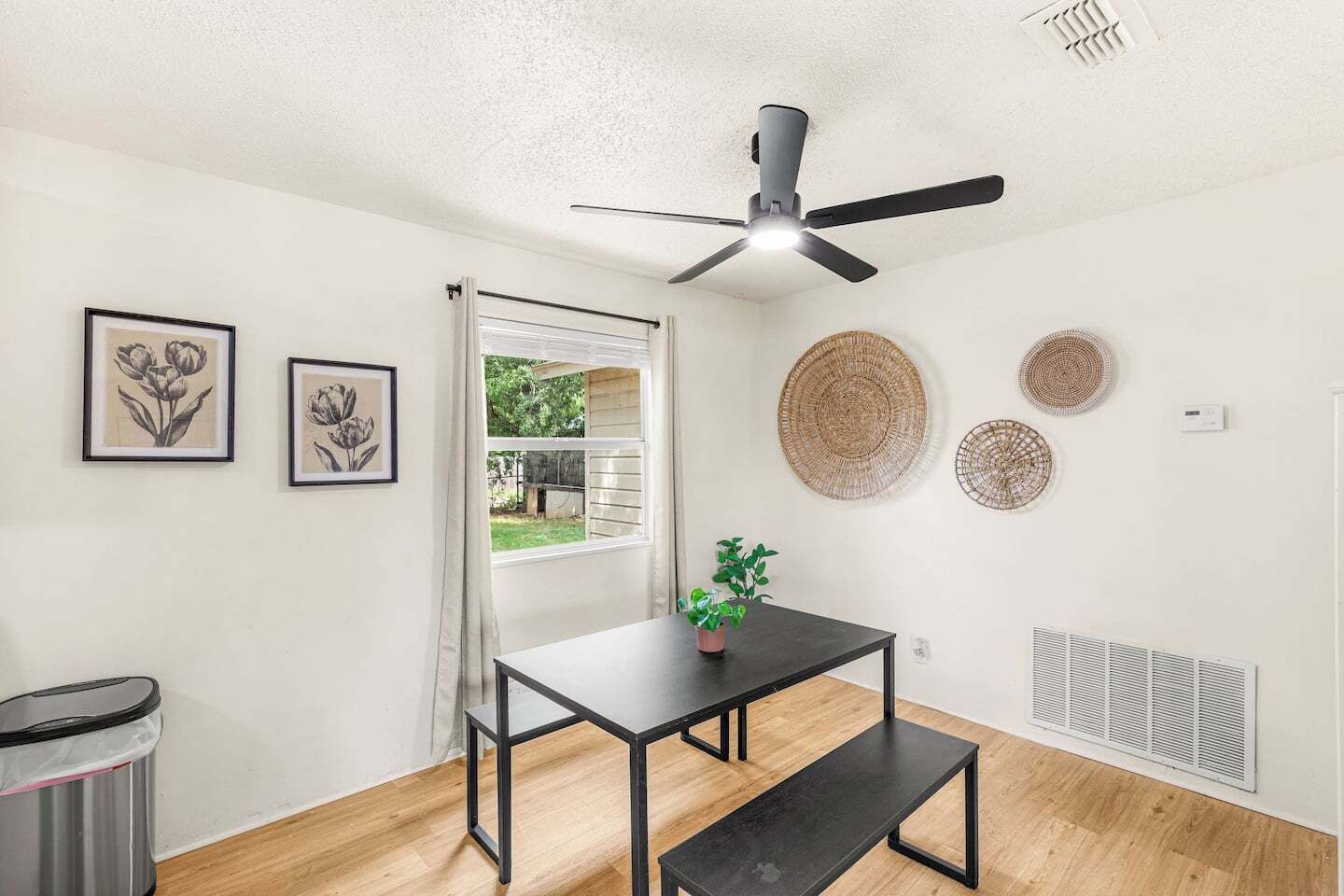 Ein Zimmer mit Deckenventilator, einem Tisch mit Blumentopf und Wandbildern.