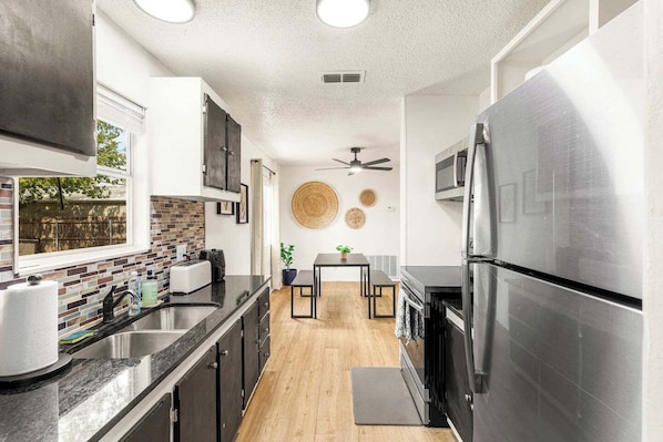 A modern kitchen with a stainless steel refrigerator, a built-in oven, and a microwave. There is a window providing a view of the outside.