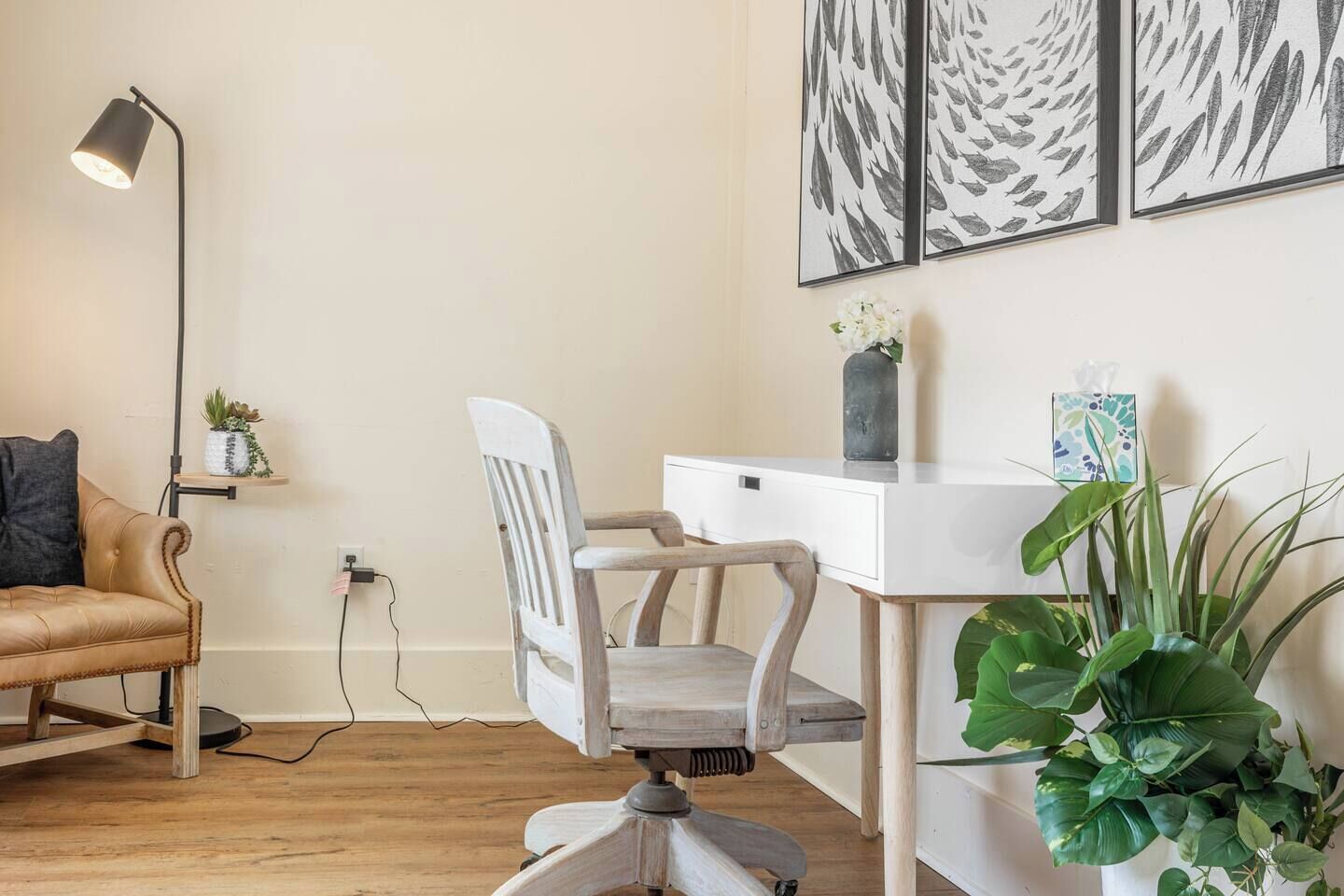 A room with a desk, chair, lamp, and artwork on the wall.