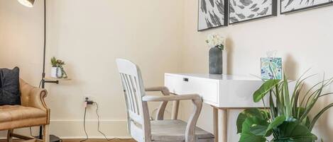 A room with a desk, chair, lamp, and artwork on the wall.
