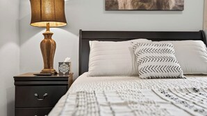 Un lit bien fait, agrémenté d’oreillers à motifs, une lampe de chevet et un tableau encadré au mur.